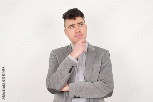 Portrait of thoughtful man keeps hand under chin, looks away trying to remember something or listens something with interest, dressed casually, poses indoors. Youth concept.