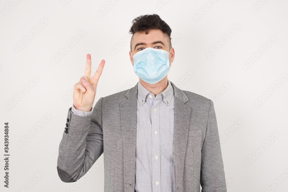 Young caucasian man standing against gray wall showing and pointing up with fingers number two while smiling confident and happy. Young caucasian man standing against gray wall showing and pointing up with fingers number two while smiling confident and happy.