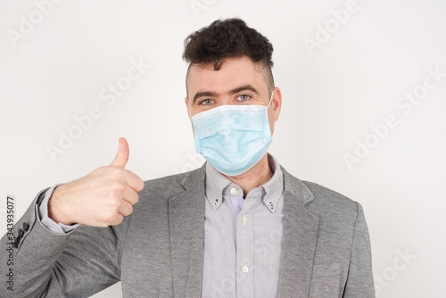 Good job! Portrait of a happy smiling blue eyed young successful man wearing medical mask giving thumb up gesture standing outdoors. Positive human emotion facial expression body language. Funny girl