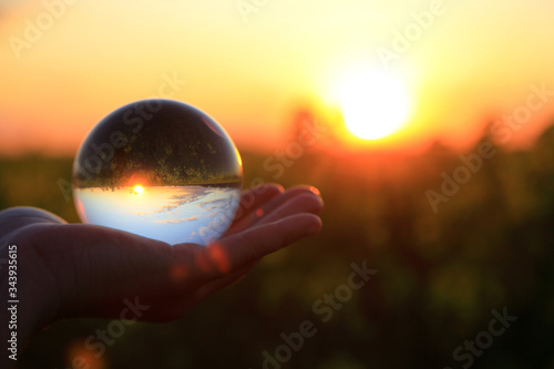 Szklana kula na dłoni w świetle zachodzącego słońca.