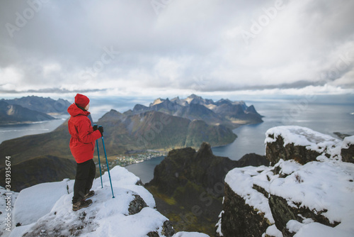 Young woman in red jacket with hiking poles on snowy mountain