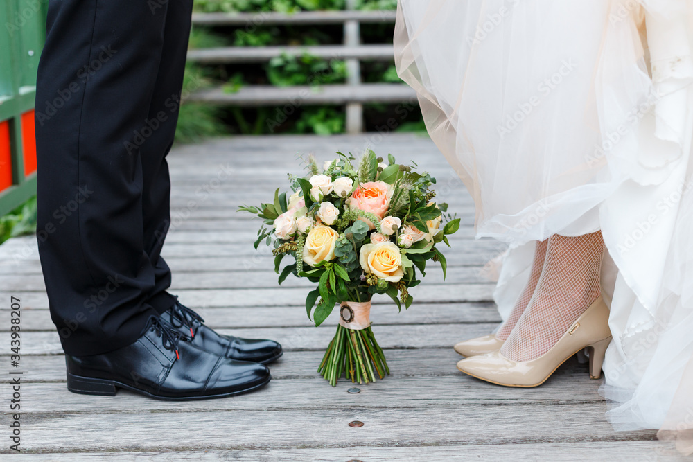 Wedding details: classic black and beige shoes of bride and groom. Bouquet of roses standing on the ground between them. Newlyweds standing in front of each other Wedding details: classic black and beige shoes of bride and groom. Bouquet of roses standing on the ground between them. Newlyweds standing in front of each other
