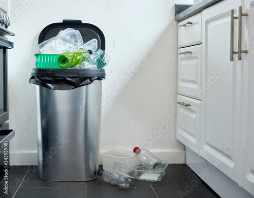 Various used plastic containers overflowing from dustin in kitchen photo