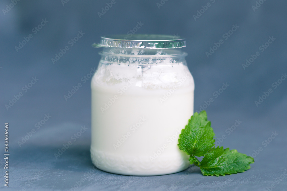 Yogurt in a glass package with mint leaves on a dark gray background. Healthy Nutrition, Essential Dairy Products