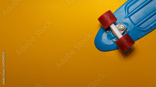 Fotografia Skateboard cruiser with blue deck and red wheels on yellow background, top view with copy-space