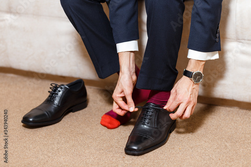 A businessman in dark blue suit, red socks and watches tying his shoelaces of black shoes. Modern, stylish and expensive look for young man