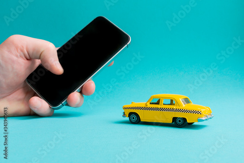 Taxi mobile online application concept.  Hand holding smart phone.Toy yellow taxi car model.