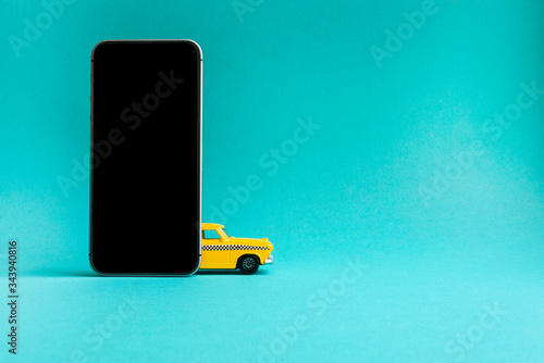 Taxi mobile online application concept. smart phone with taxi service app on display.Toy yellow taxi car model.