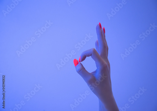 Woman hand with bright orange manicure showing gesture OK in neon light.
