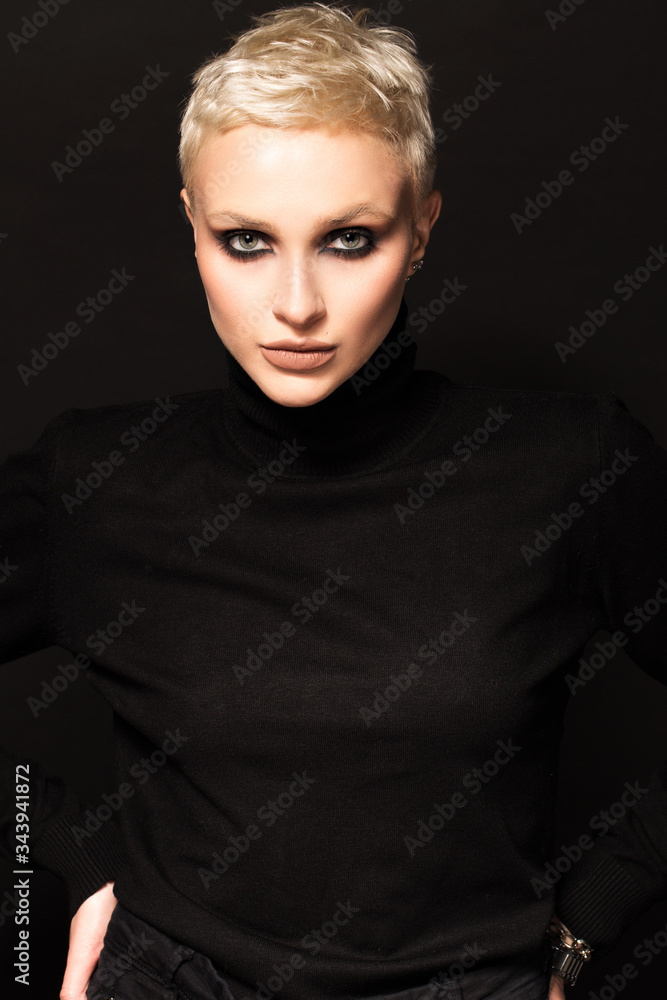 Short-haired blonde in black clothes on a black background.