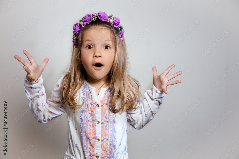 Portrait of pretty little girl in white dress and purple wreath on gray isolated background. Wonder and wow emotion concept Portrait of pretty little girl in white dress and purple wreath on gray isolated background. Wonder and wow emotion concept