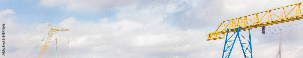 Machine crane and bridge crane on a background of blue sky with clouds, panoramic view, high resolution