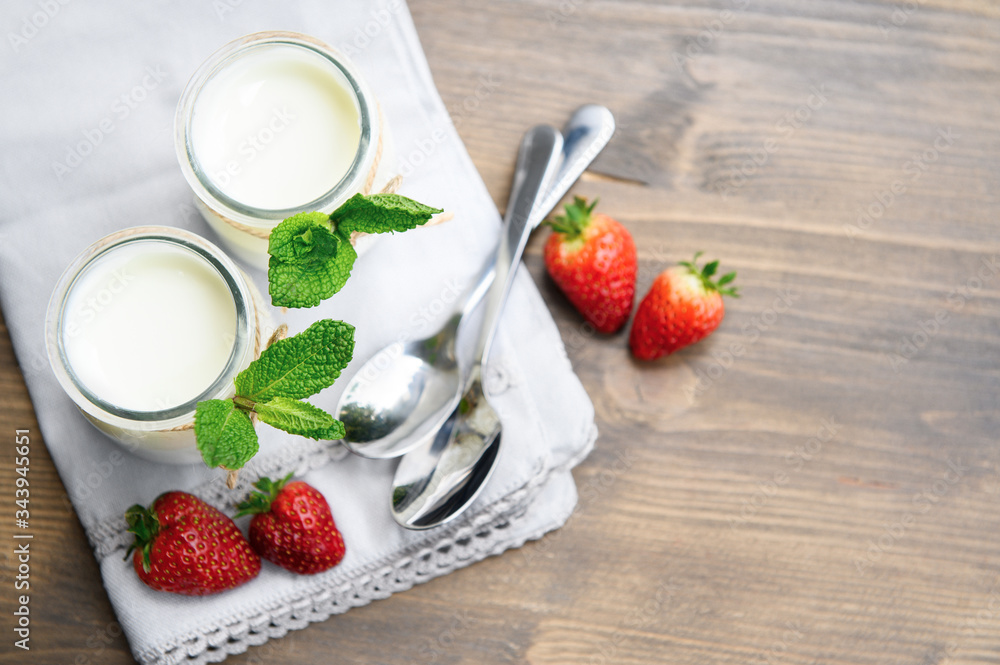 Two glasses of natural yogurt on a wooden table are decorated with mint and strawberries. Two glasses of natural yogurt on a wooden table are decorated with mint and strawberries.