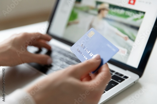 Close up of young woman hold bank credit card paying online making purchase on laptop, female enter account details in Internet service system, shopping on Internet using computer browser application