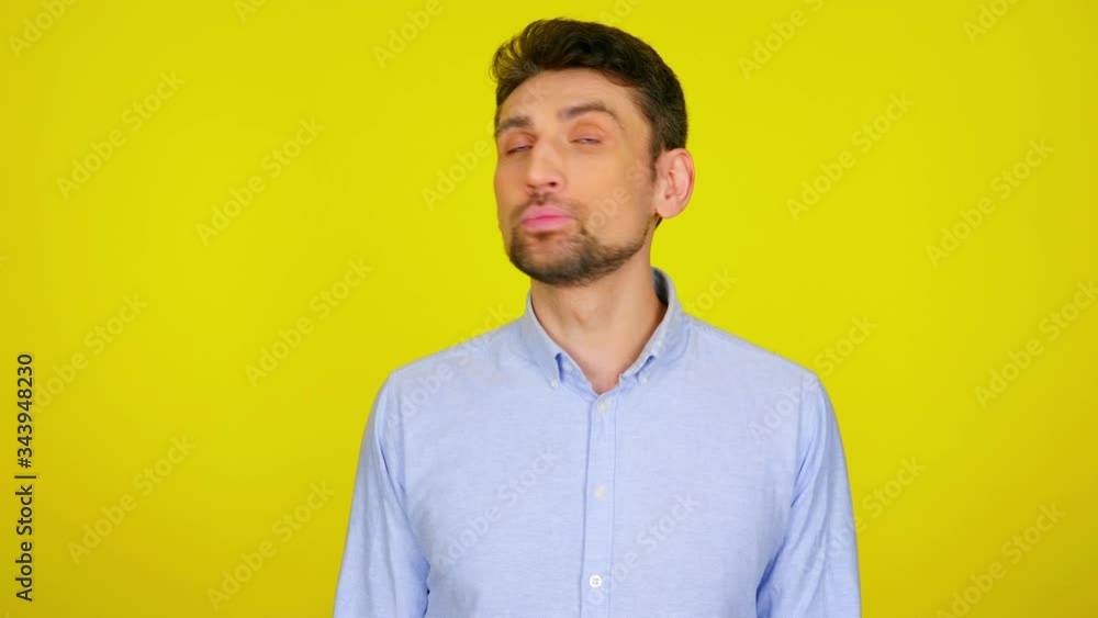 Young man in light blue shirt is looks around at places for text and shrugs, don't knows what to choose. Yellow background with copy space. Human emotions. 4k footage Young man in light blue shirt is looks around at places for text and shrugs, don't knows what to choose. Yellow background with copy space. Human emotions. 4k footage