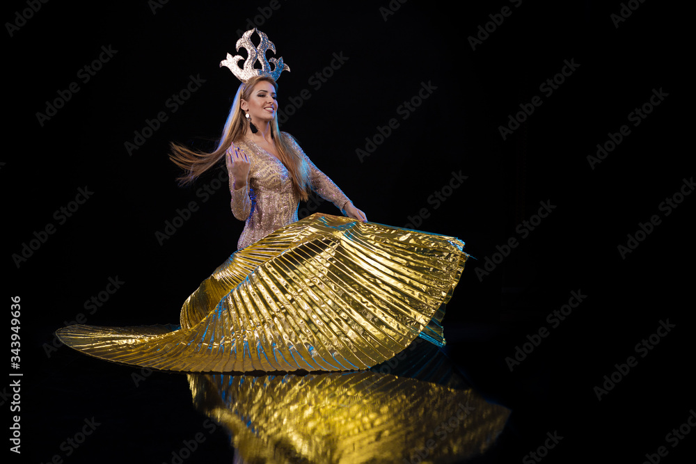 Young woman dancer in a gold dress and with a golden crown on her head ...