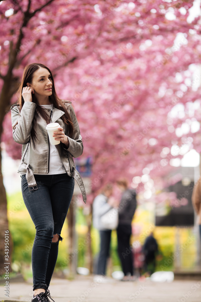 Woman in good mood posing with cup of coffee against sakura tree Woman in good mood posing with cup of coffee against sakura tree