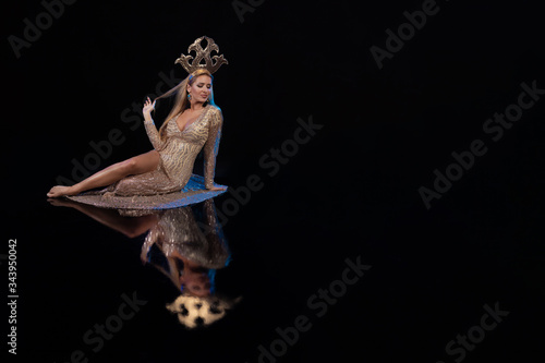 Young woman dancer in a gold dress and with a golden crown on her head on a black background