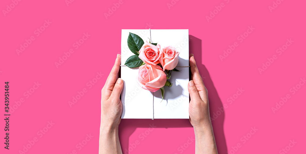 Female hands holding a gift box with pink roses overhead view - flat lay Female hands holding a gift box with pink roses overhead view - flat lay