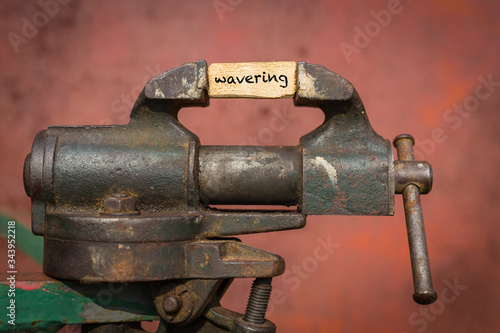 Vice grip tool squeezing a plank with the word wavering