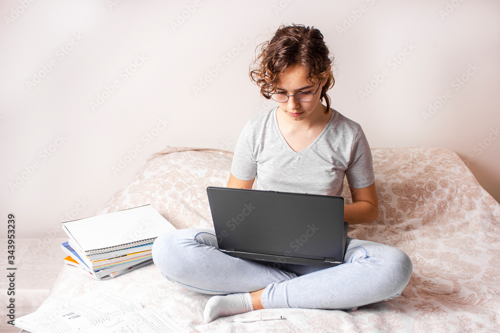 Pretty curly teenager girl studying online on the bed with lap top computer Pretty curly teenager girl studying online on the bed with lap top computer