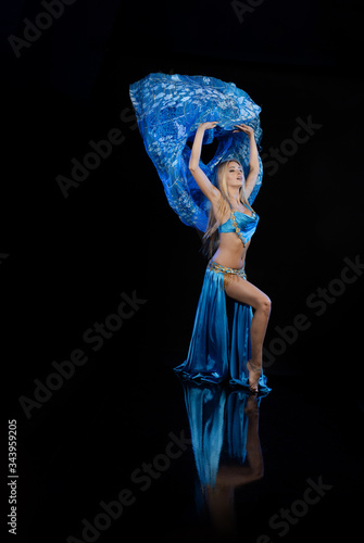 Young woman belly dancer in a blue oriental costume on a black background photo