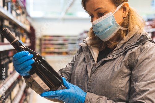 Young woman choosing bottle of wine during lockdown.  Protection and prevent measures while shopping. Covid-19 virus pandemic safety measure. Self isolating and self distancing during pandemic. photo