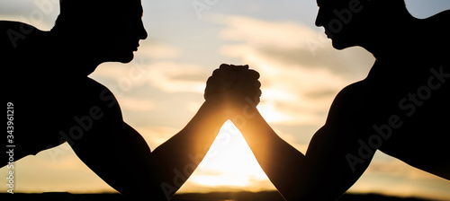 Two men arm wrestling. Silhouette of hands that compete in strength. Rivalry, vs, challenge, strength comparison. Sunset, sunrise. Rivalry, closeup of male arm wrestling. Men measuring forces, arms