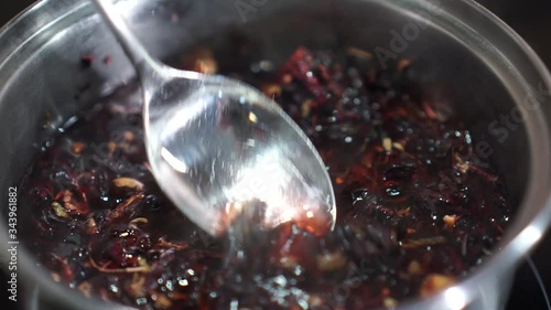 Red tea Hibiscus sabdariffa rose petals herbal infusion boiled in silver pot spoon stir