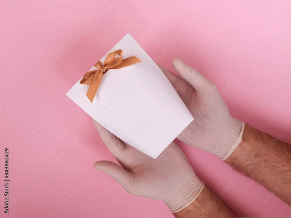 Male hands in glove holding a white gift bag on a pink background. Male hands in glove holding a white gift bag on a pink background.