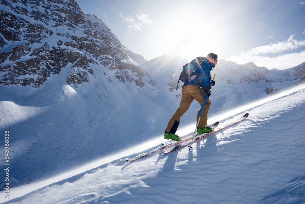 © Cavan Images - Man ski touring uphill in the wind and backlit by sun