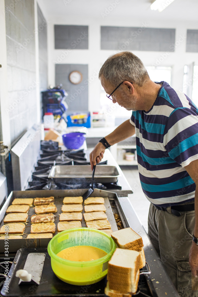 Elderly man cooking french toast in industrial kitchen.