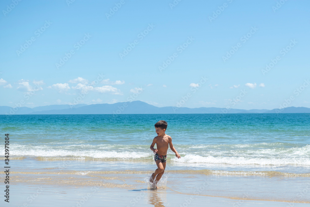 Little boy running on beach beside blue sea in a sunny day of summer.