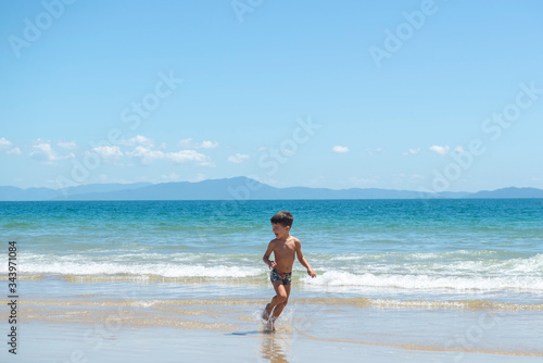 Little boy running on beach beside blue sea in a sunny day of summer.