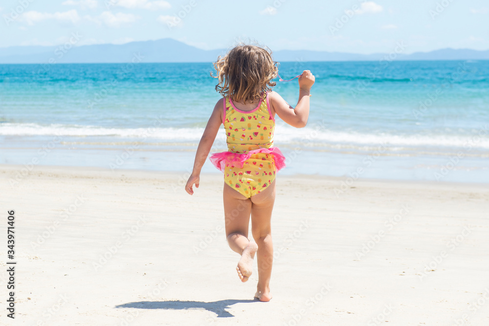 Back view of girl running in swimsuit on the beach towards the blue sea on beautiful sunny day. Back view of girl running in swimsuit on the beach towards the blue sea on beautiful sunny day.