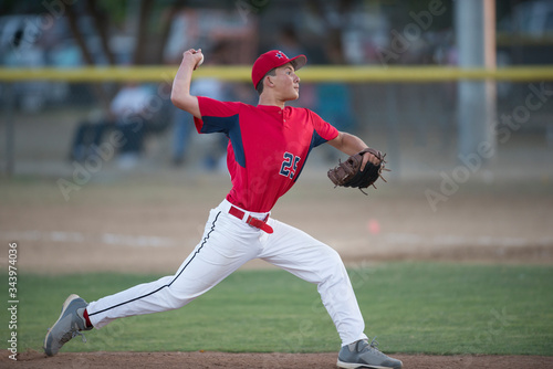 teen baseball player pitcher in red uniform in full wind up on the mound photo