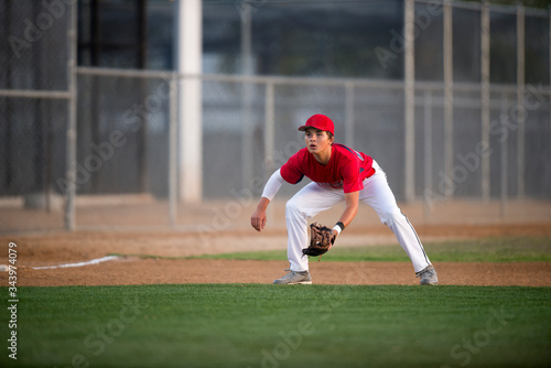 Teen baseball player in red uniform ready for a ground ball photo