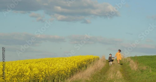 Happy family concept. Mom and baby hold hands and walk in evening in field in rays of beautiful sunset. Little daughter in a black dress walks with her mother in yellow dress on road. happy family tra photo