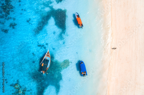 Aerial view of the fishing boats in clear blue water at sunset in summer. Top view from of boat, yacht, sea and walking man on the sandy beach in Zanzibar. Travel. Tropical seascape. View from above © den-belitsky