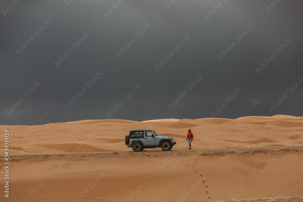 woman walks back to jeep under stormy skies in utah sand dunes woman walks back to jeep under stormy skies in utah sand dunes