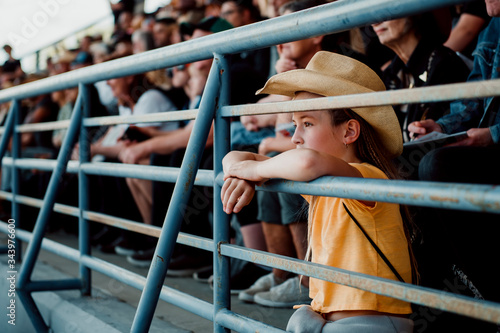 Girl watching rodeo while sitting on railing photo