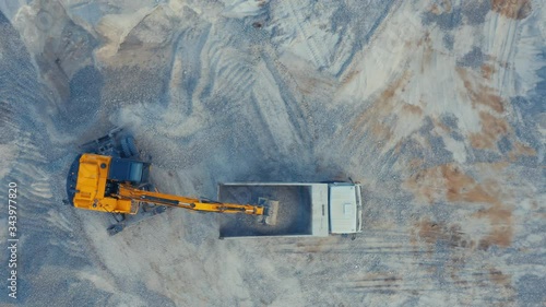 Aerial top down view of an excavator loading crushed stone into a dump truck in a crushed stone quarry