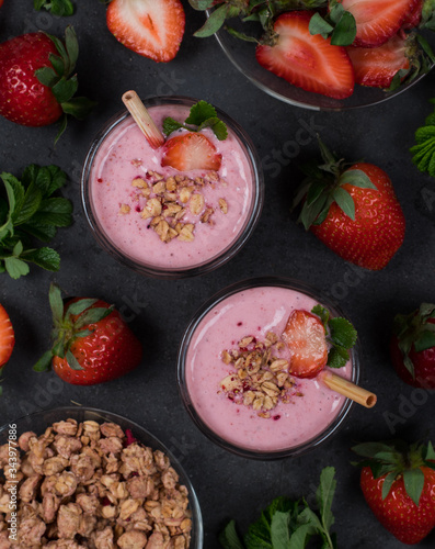 Strawberry smoothie with granola and nuts in a glass with a bamboo straw on a dark background top view