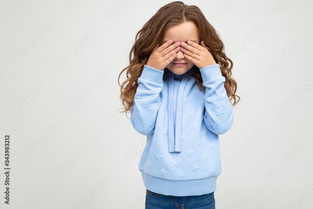 European teenage girl in a blue hoodie covered her eyes with her hands on a white background with copy space European teenage girl in a blue hoodie covered her eyes with her hands on a white background with copy space