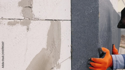 Worker glues insulation on the wall of the house