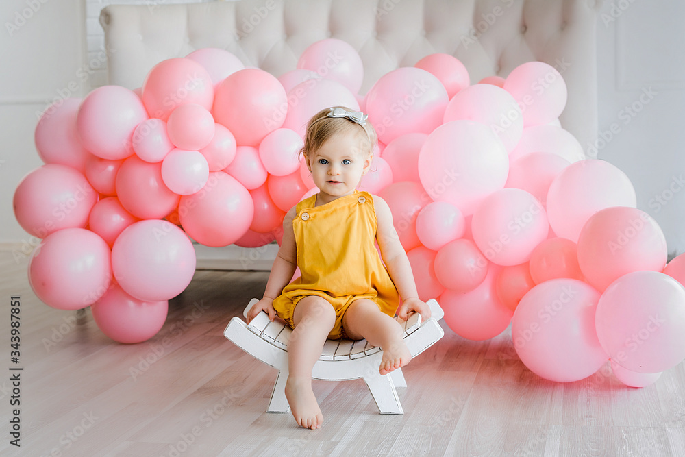 Handsome baby girl with golden hair dressed yellow romper sitting on small white bench. Happy moments, pink balloons. Cute and pretty little kid, first birthday . Handsome baby girl with golden hair dressed yellow romper sitting on small white bench. Happy moments, pink balloons. Cute and pretty little kid, first birthday .