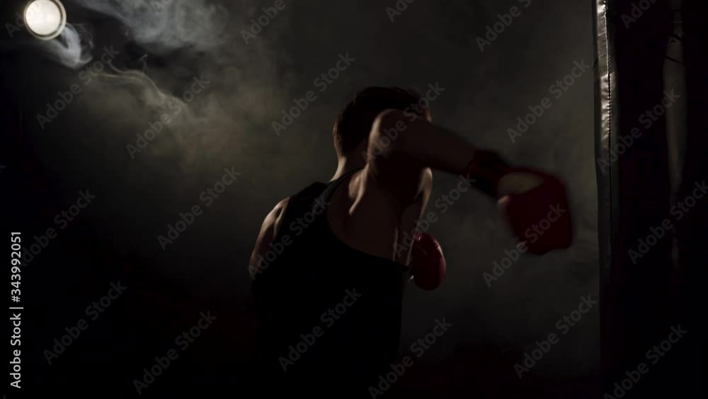 Young boxer is practicing blows on a punchbag. Young fit boxer during a workout. Kickboxer punching a punchbag in a gym Young boxer is practicing blows on a punchbag. Young fit boxer during a workout. Kickboxer punching a punchbag in a gym