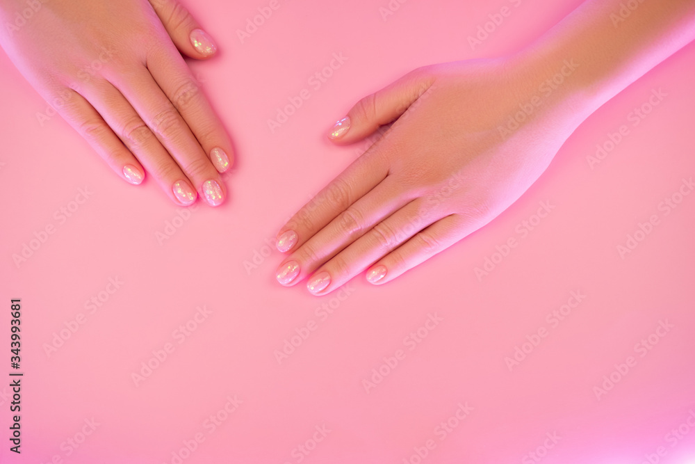 Stylish nude female manicure. Beautiful young woman's hands in trendy neon light on pink background. Beauty concept.