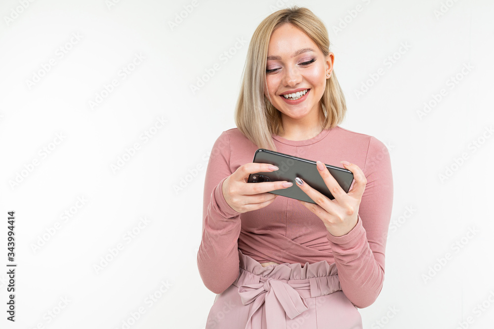 Caucasian blond girl in pink clothes plays on the phone in a horizontal position on a white background with copy space Caucasian blond girl in pink clothes plays on the phone in a horizontal position on a white background with copy space