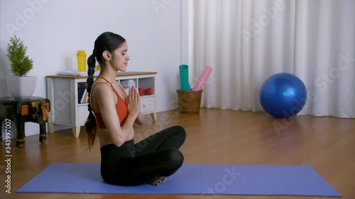 A young attractive female practicing yoga in sportswear on a blue yoga mat at home. Flexible Indian girl performing Janu Sirsasana (head-to-knee forward bend) and Krounchasana (modified heron pose) photo